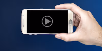 Image of a man's hand holding a smart phone with a video loaded and ready to play on the screen.