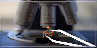 Photo of a microscope with an illustrated graduation cap being placed on the tray using tweezers.