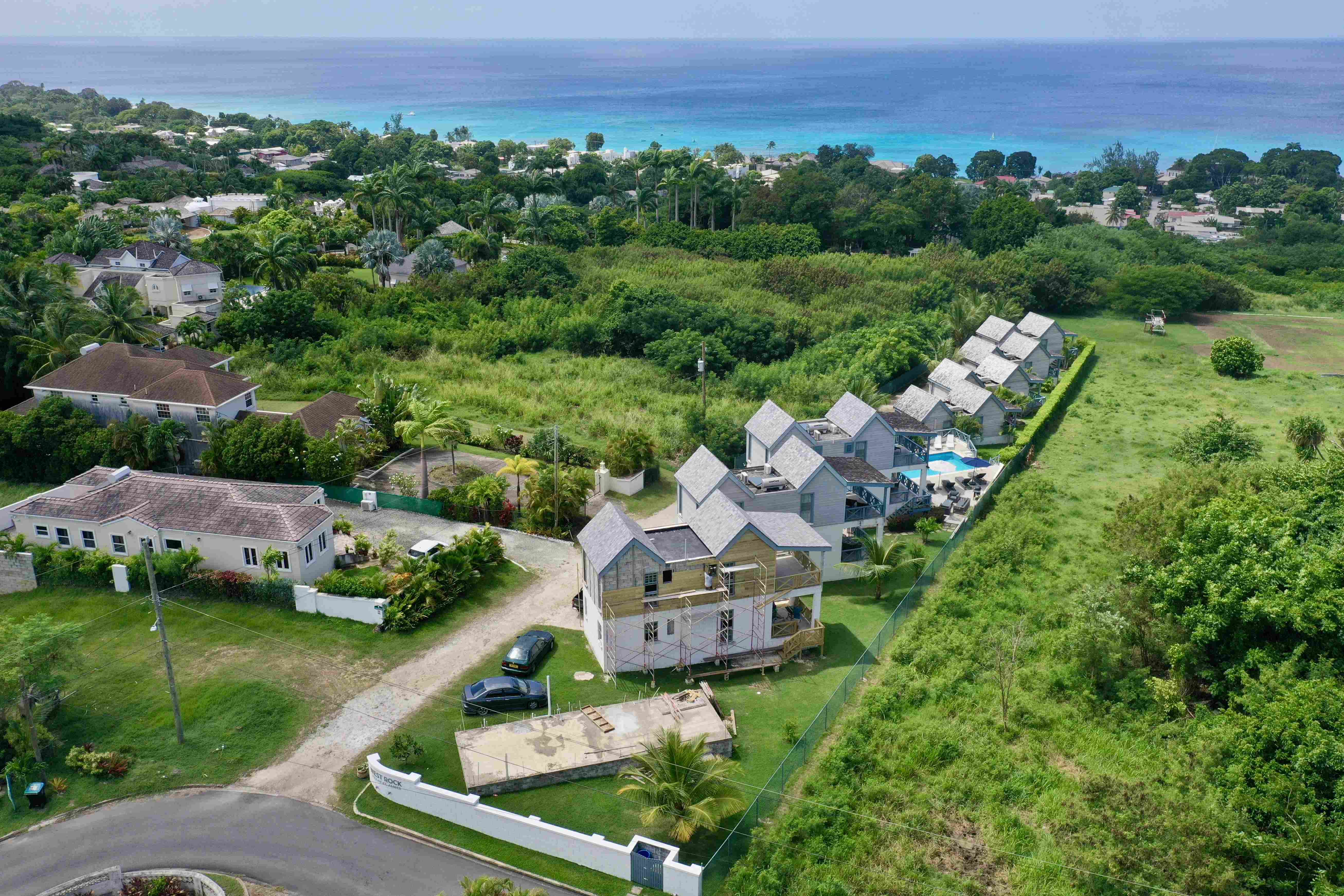 Aerial view of a coastal residential area with houses, lush greenery, and the ocean in the background.