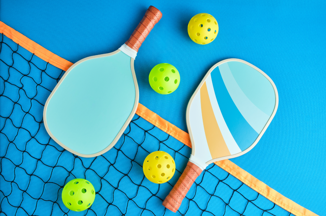 Two pickleball paddles on a court laying on a net with 4 pickleballs spread out between them