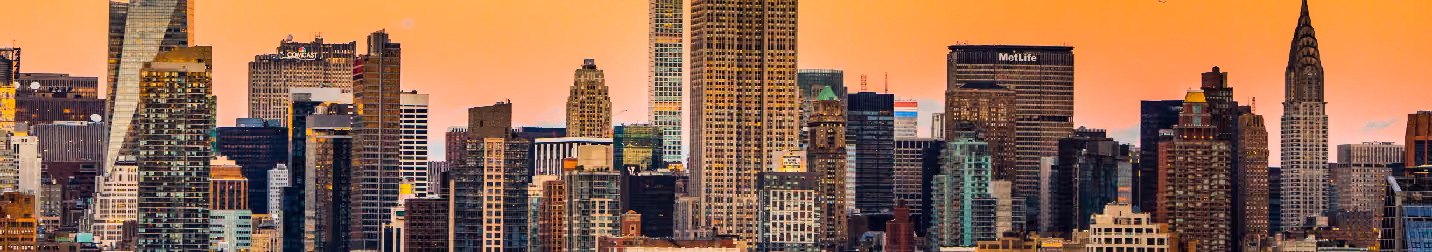 Panoramic view of New York City skyscrapers at sunset, featuring the Empire State and Chrysler buildings.