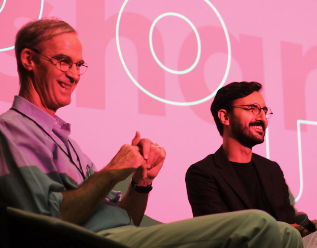 Two men sitting and smiling on stage
