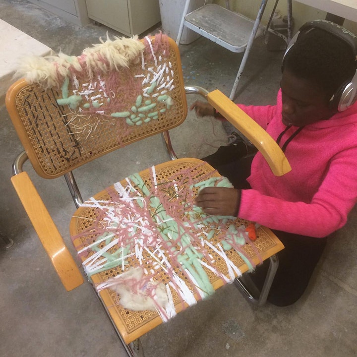 person on their knees adding embellishments to a woven chair