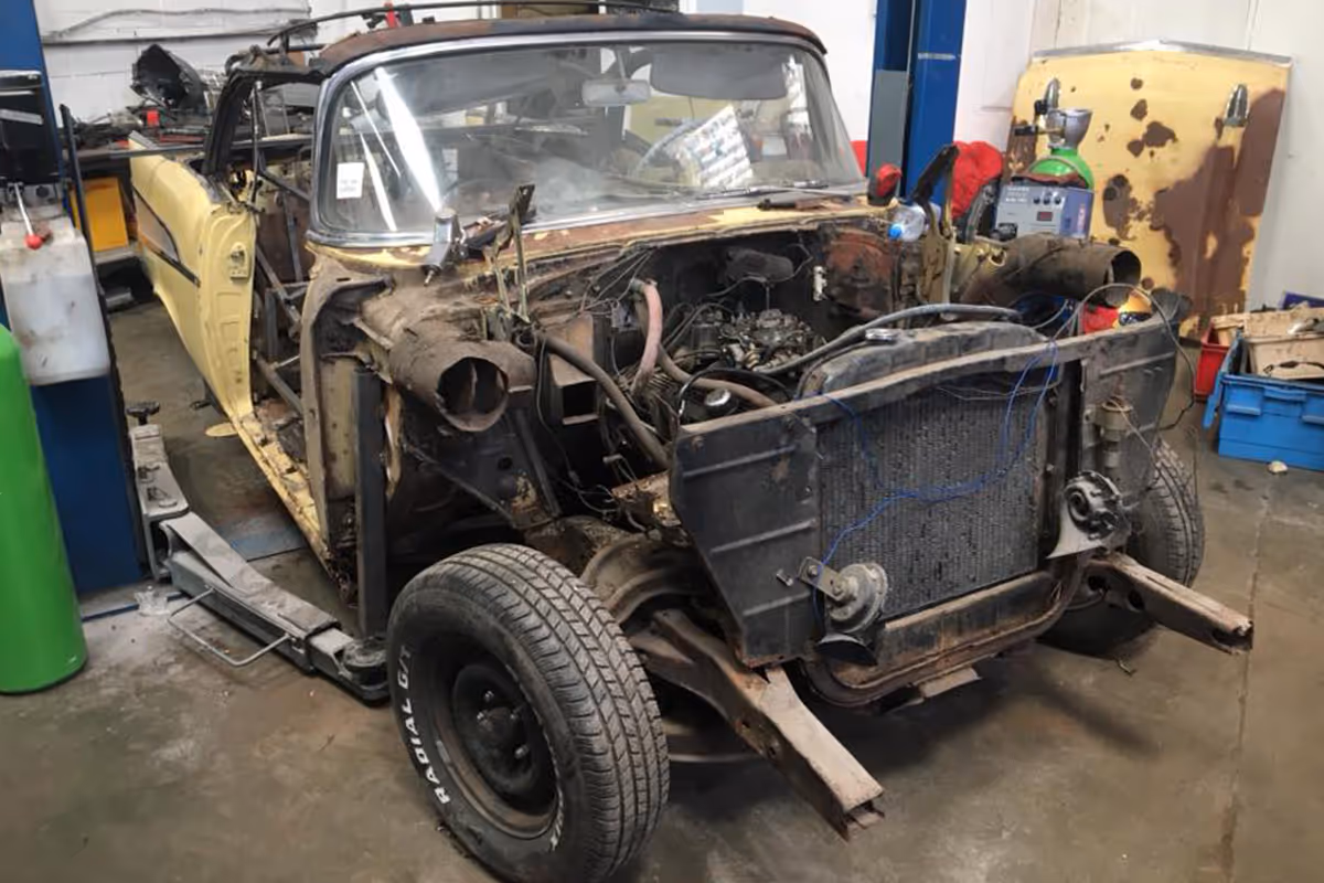 A partially dismantled vintage car under repair in a workshop.