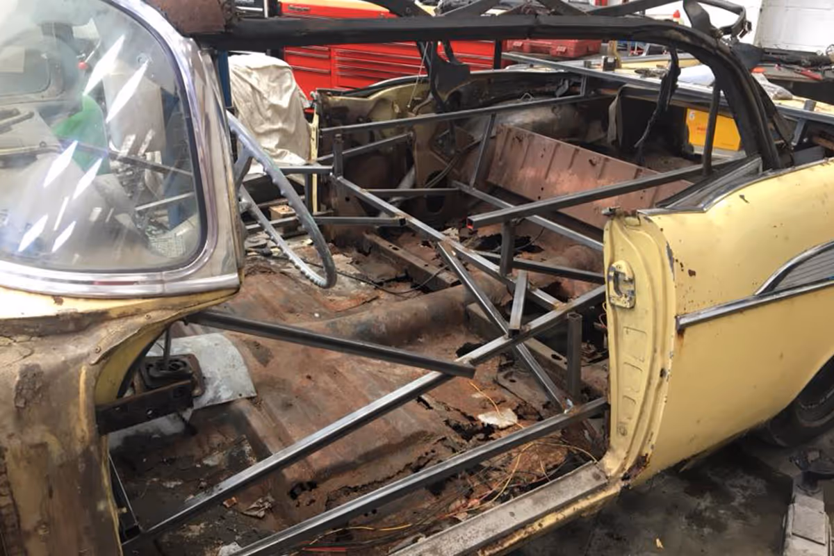 A partially stripped vintage car with visible interior metal framework in a workshop.