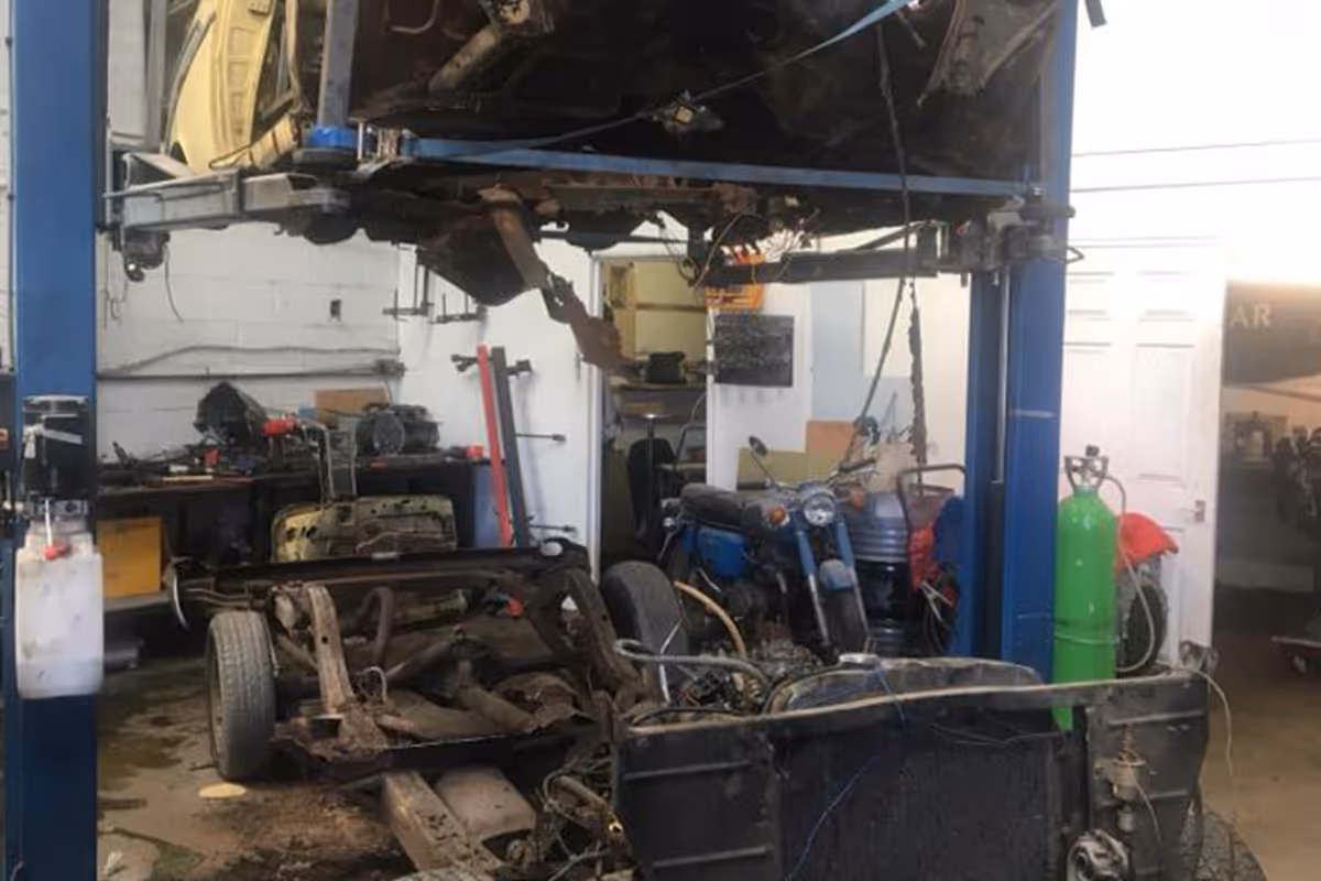 A vehicle is being repaired on a lift with exposed parts in a cluttered garage.
