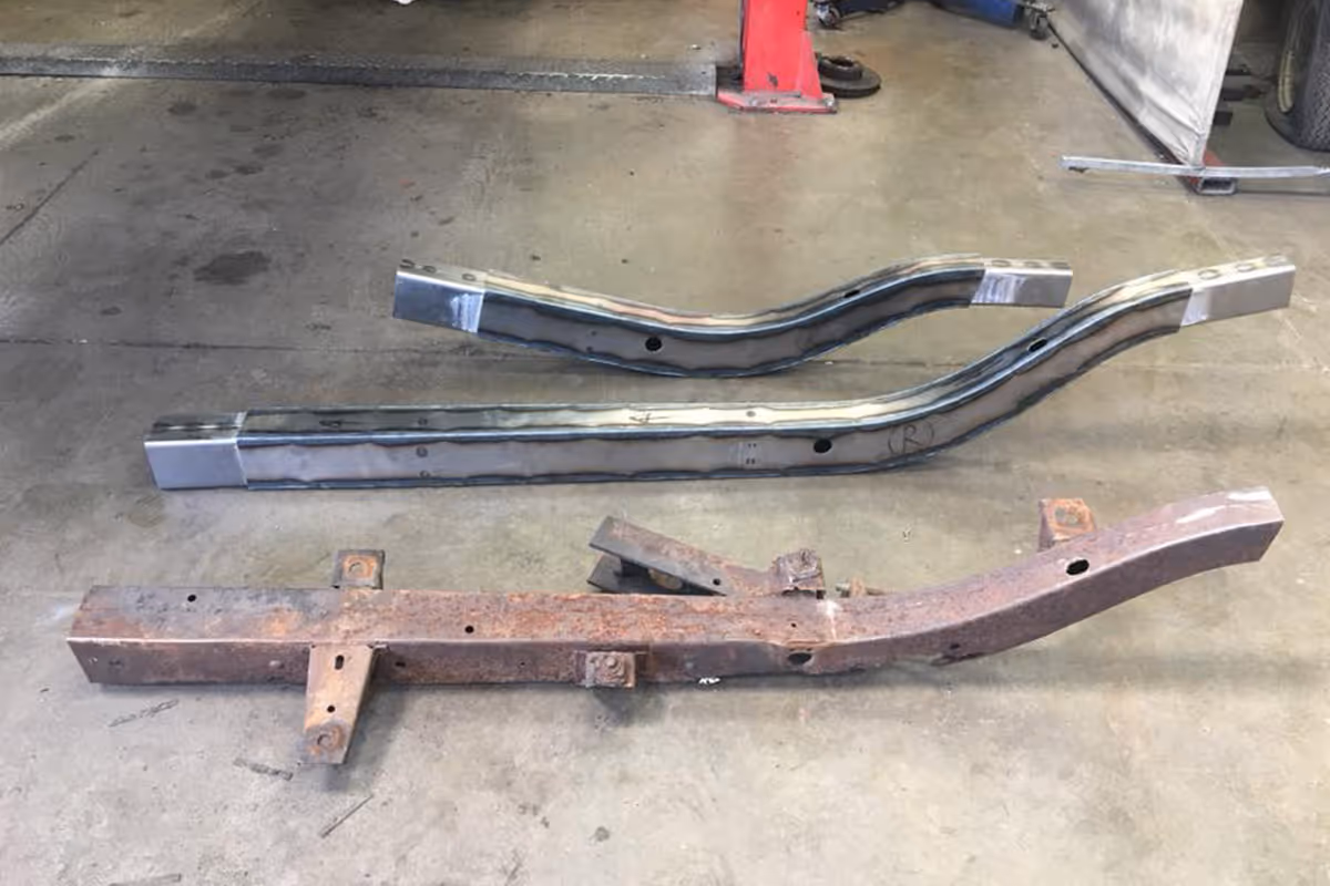 Three metal car frame reinforcement rails on a garage floor, two new and one rusted.