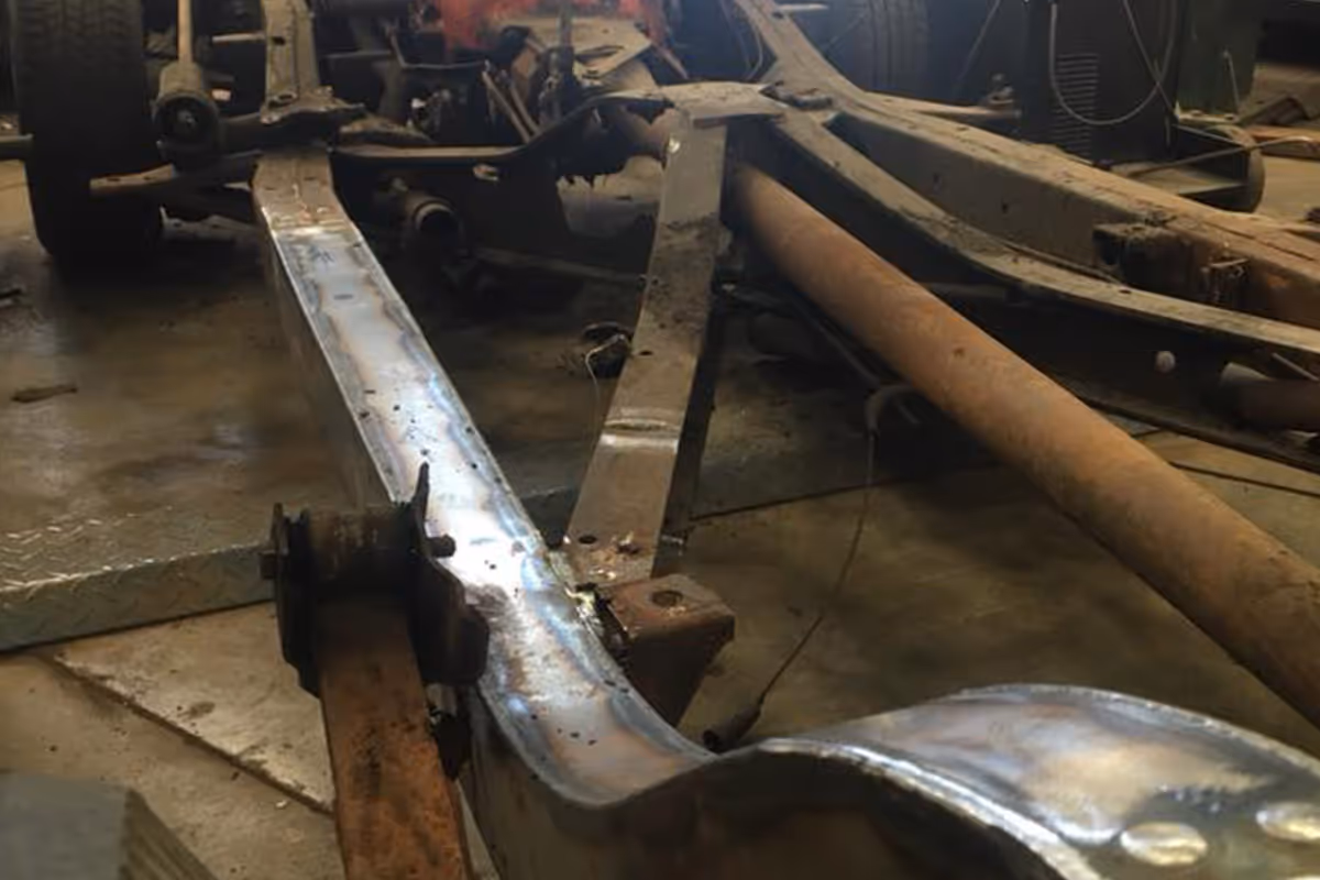 A car chassis is being repaired in a workshop setting, with visible metal parts and tools.