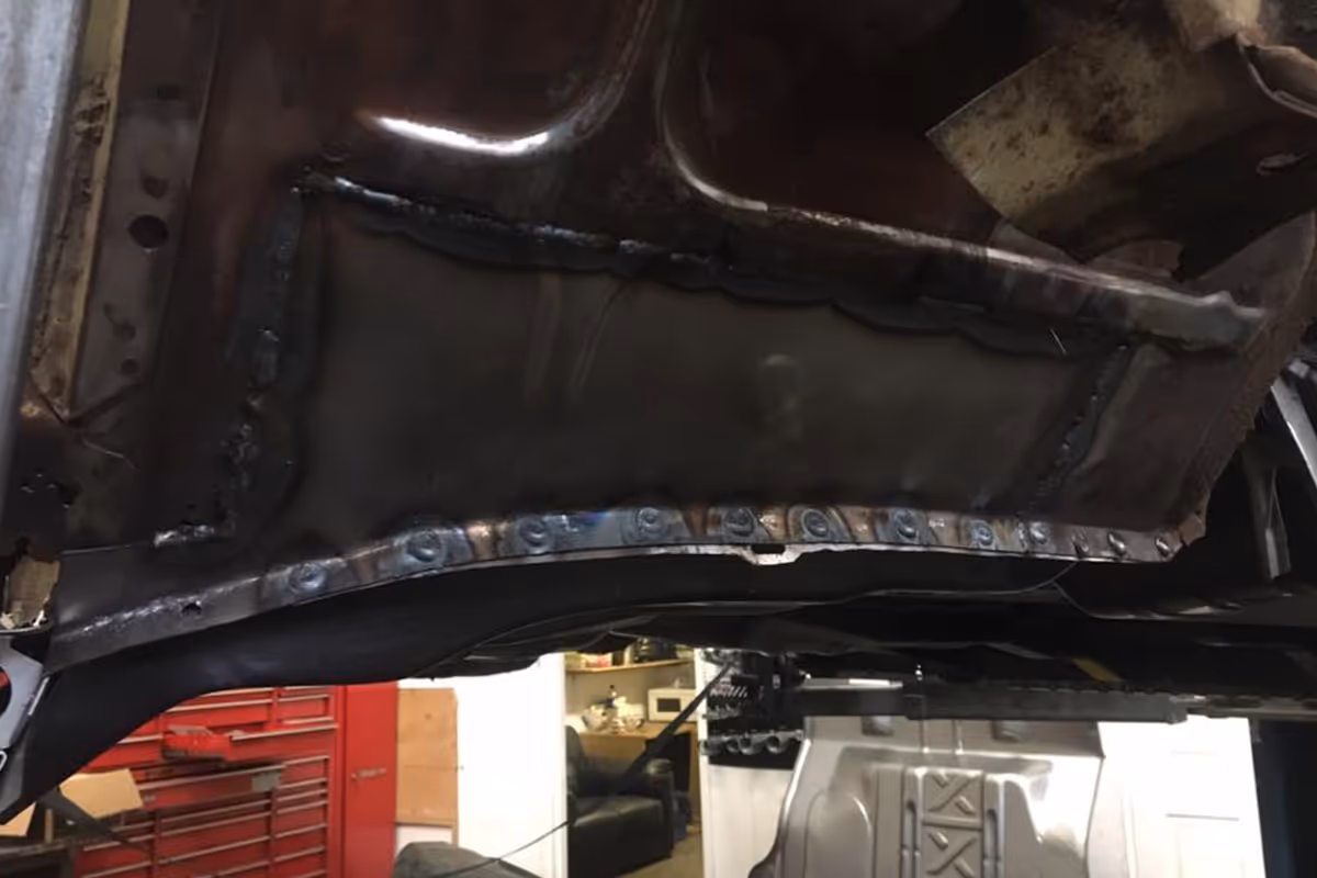 A welded metal panel repair is visible inside a vehicle, with some tools in the background.