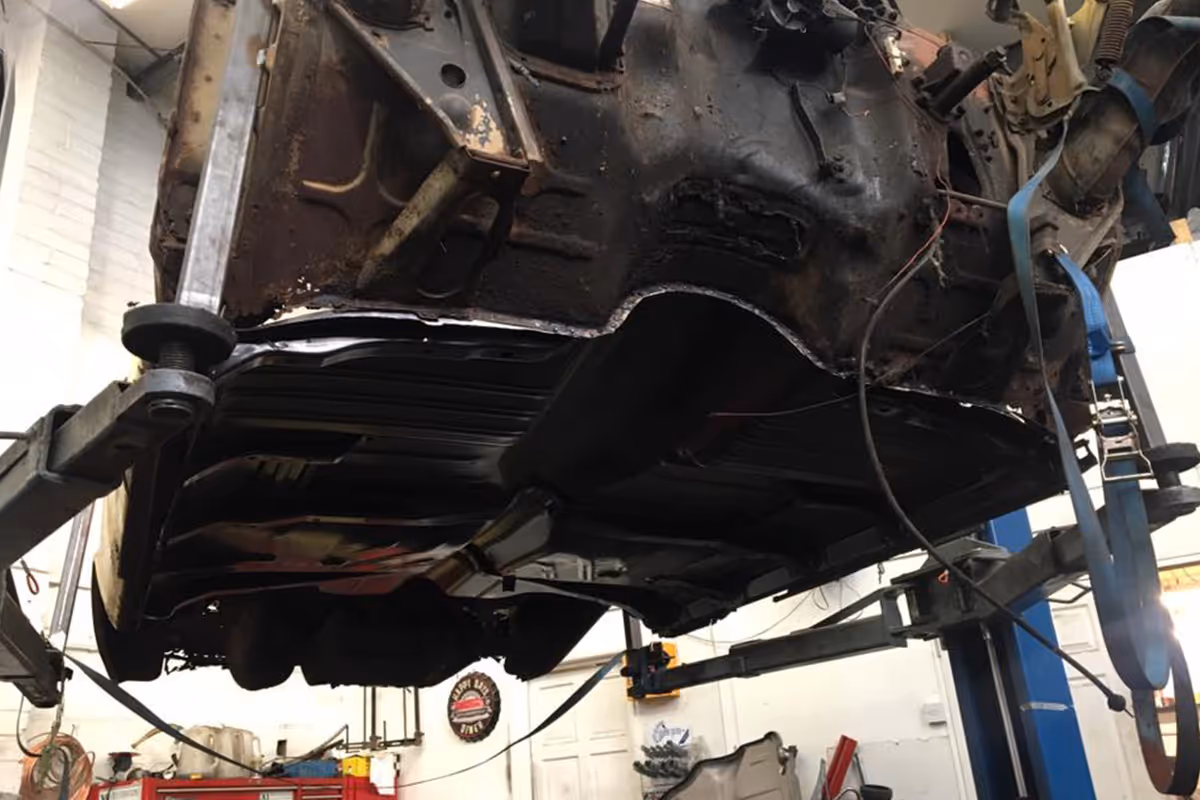 A car chassis is mounted on a lift in a garage, undergoing repair work.