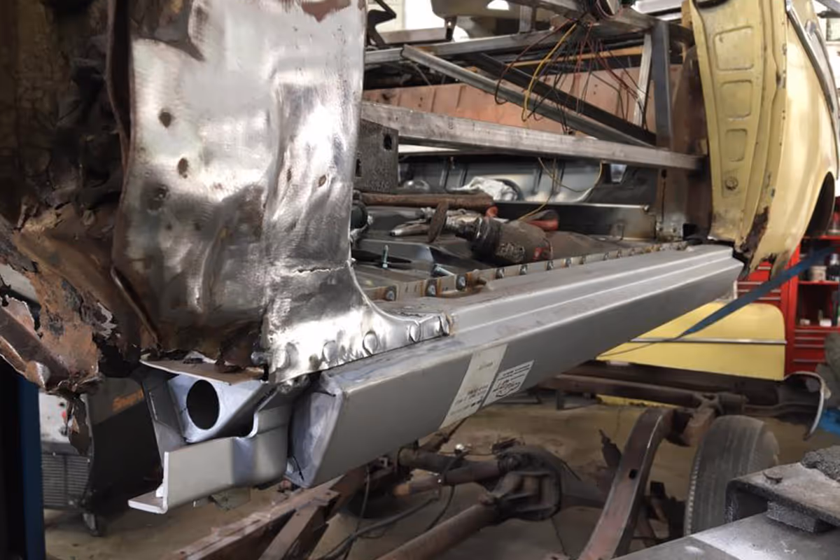 Close-up of a partially restored car body with new metal paneling welded onto the frame.