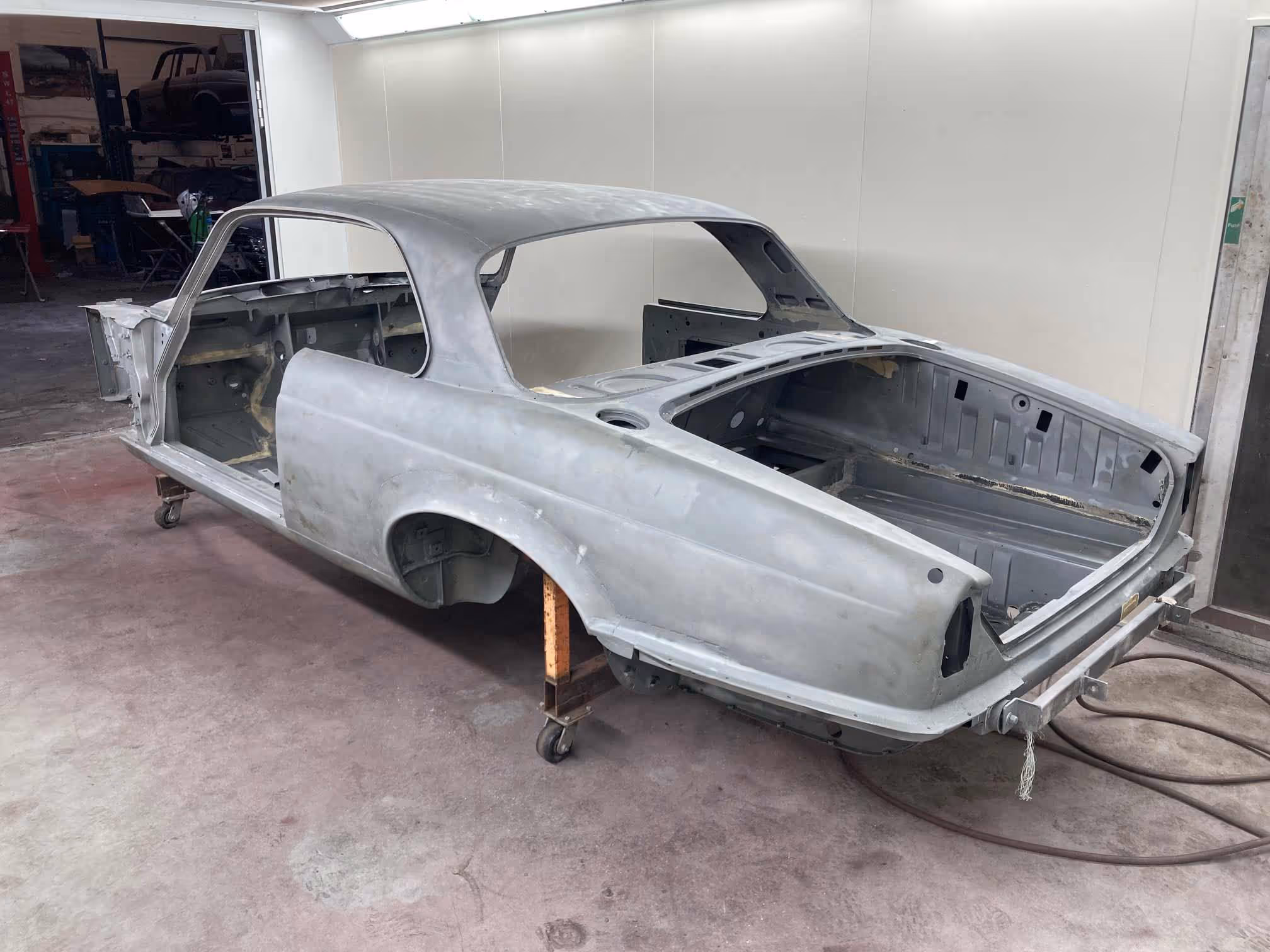 A stripped-down car body on stands is in a workshop for restoration.