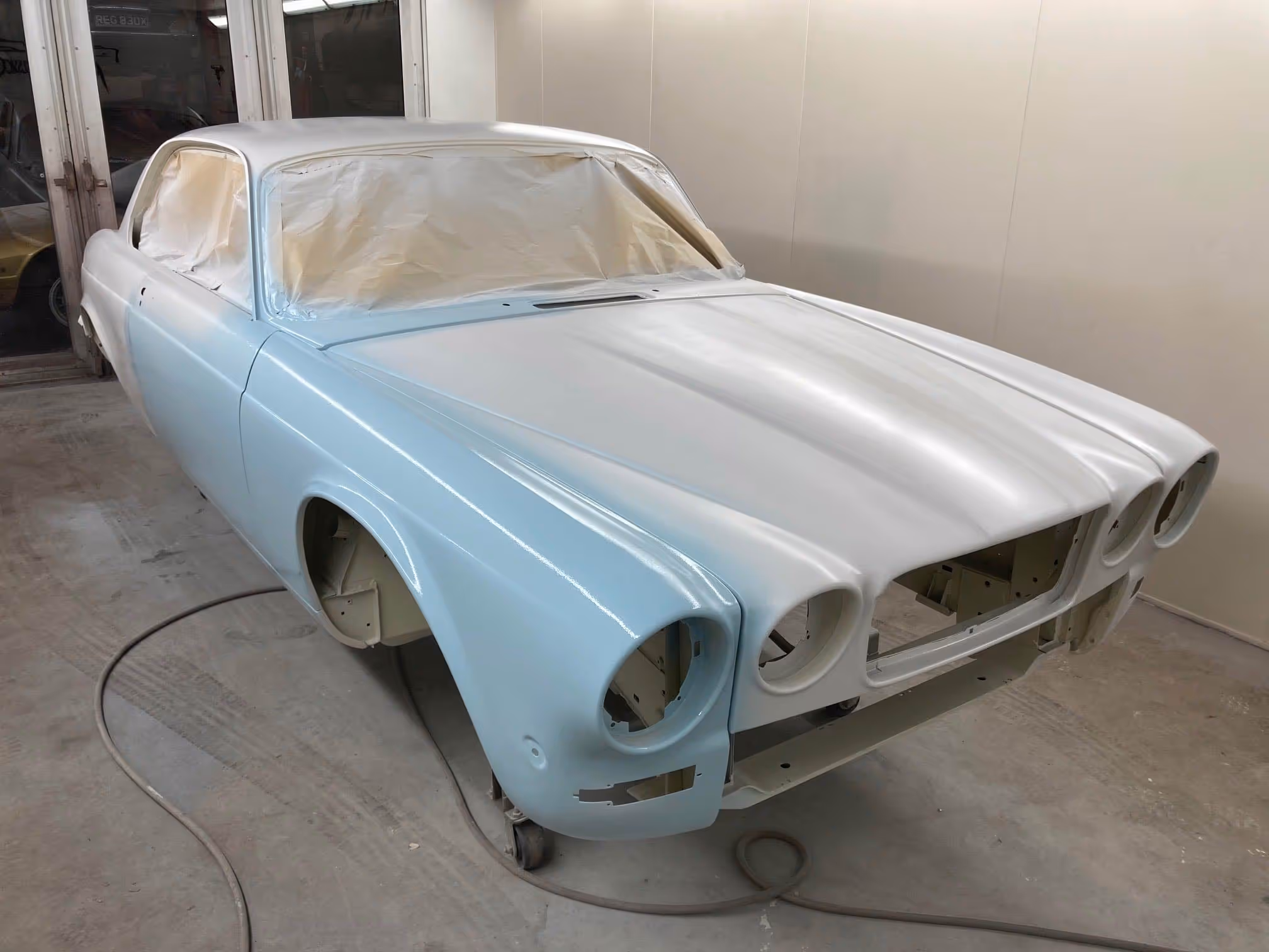 A classic car is being repainted in a light blue and white color inside a garage.