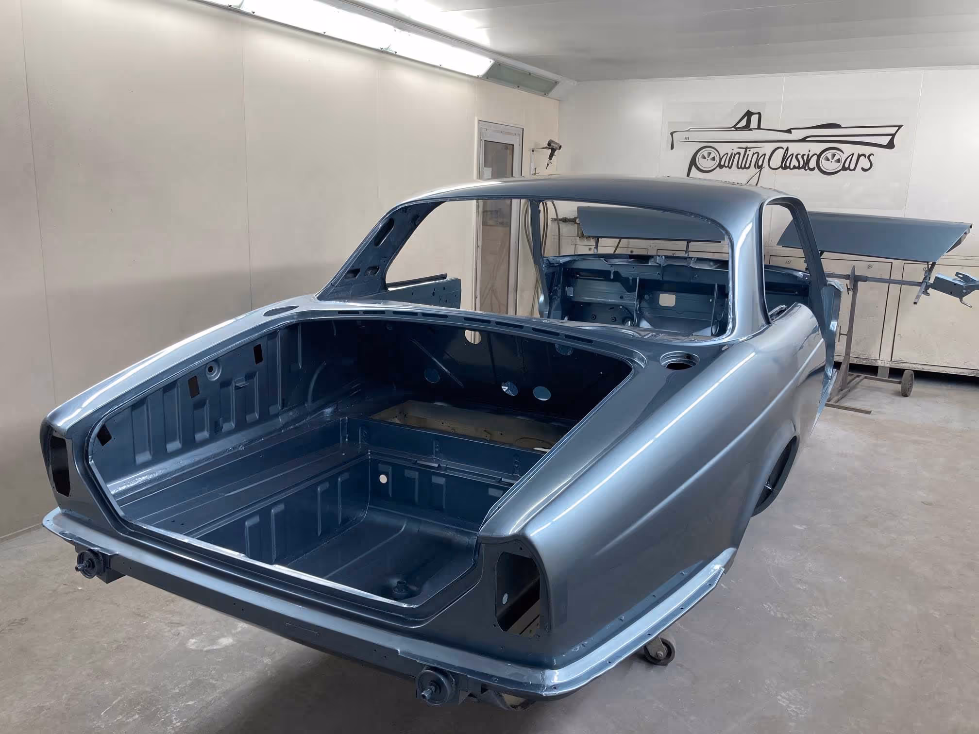 A classic car is being restored in a workshop, with its body freshly painted in metallic blue.