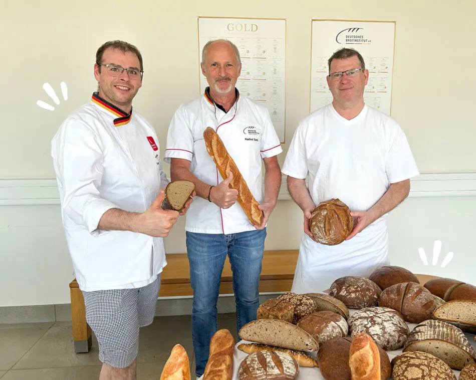 Drei Männer halten jeweils ein Brot in der Hand und lachen in die Kamera.