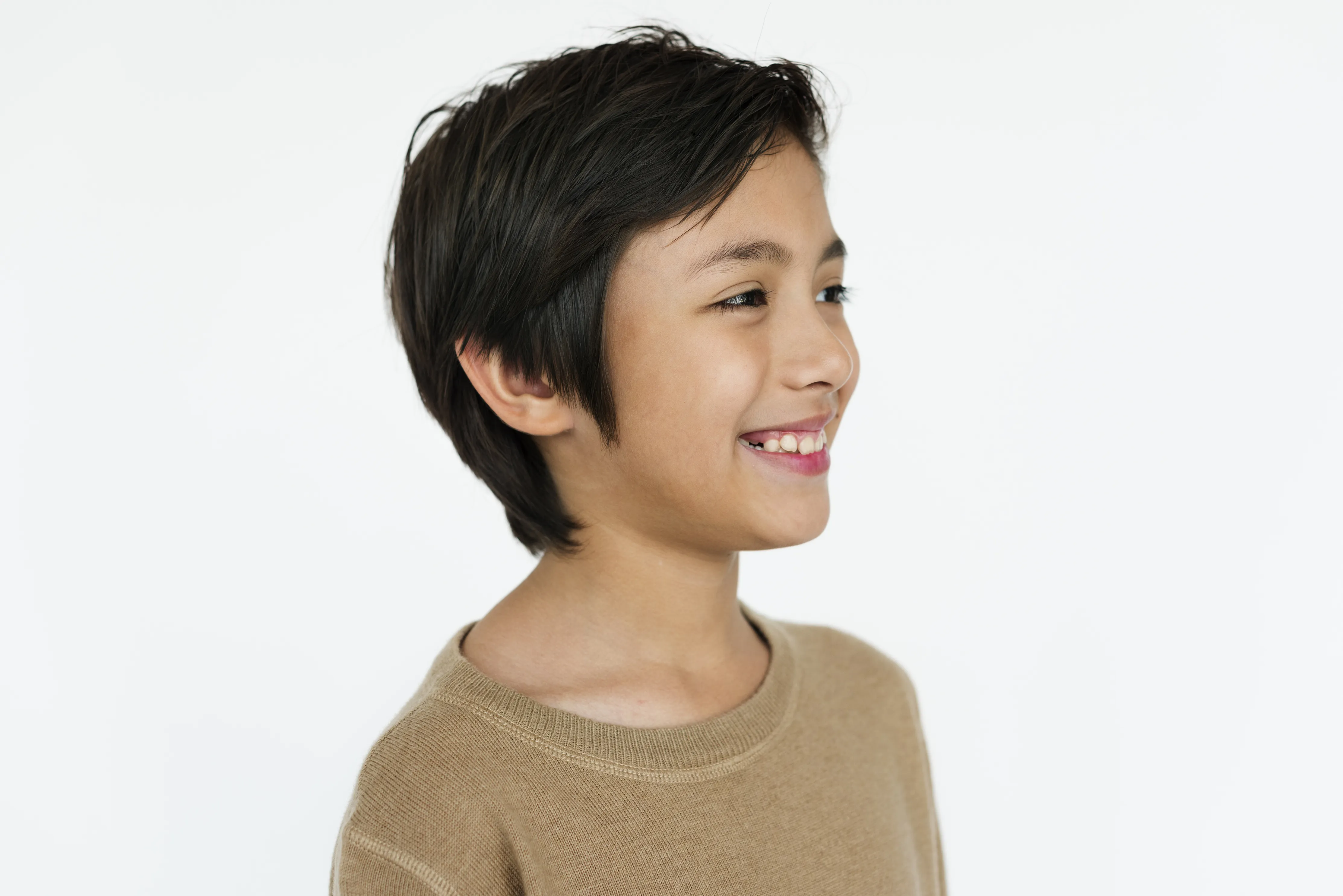 Smiling young person with short dark hair wearing a beige sweater, shown in profile on a white background.