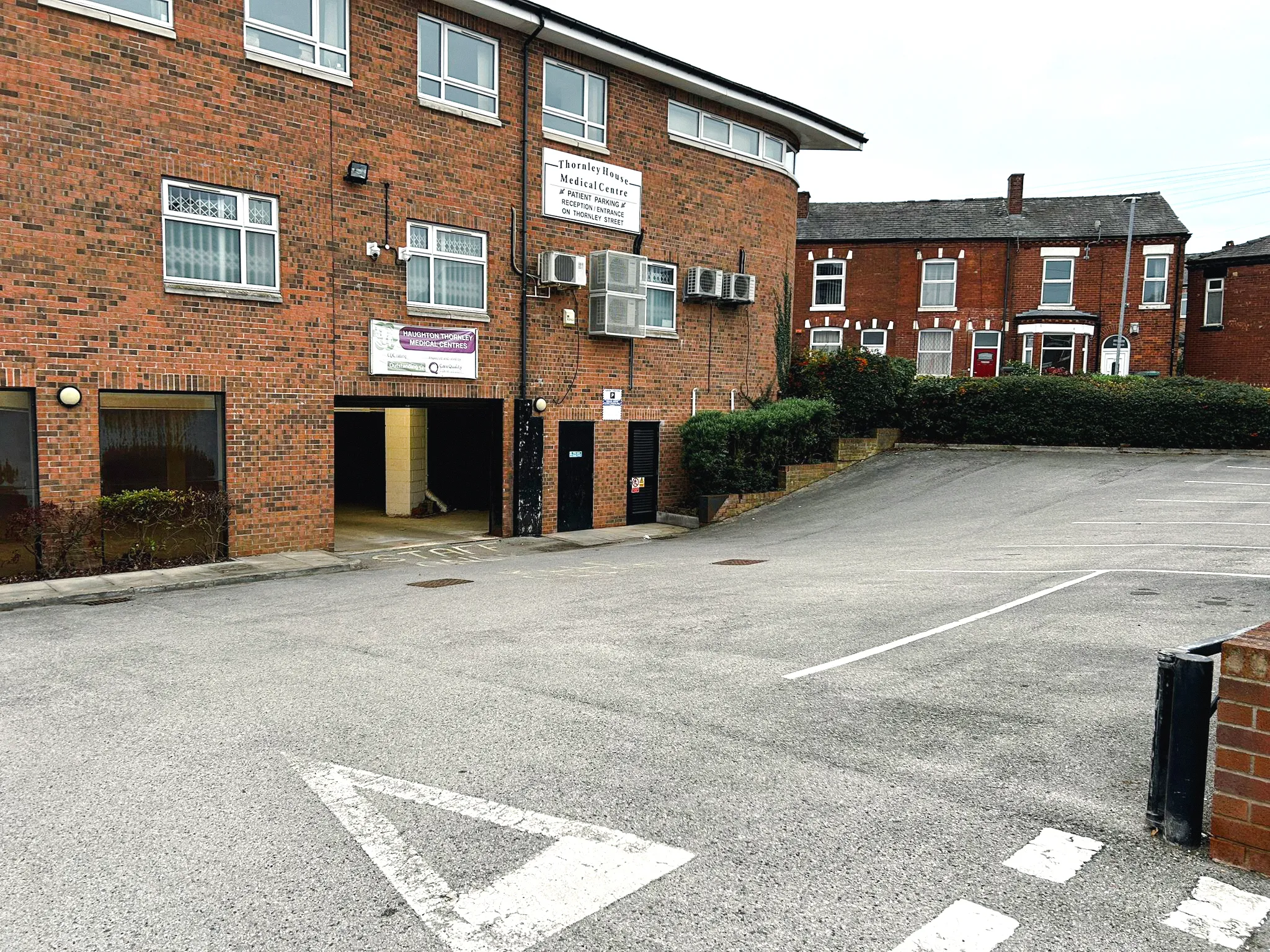 Empty parking lot in front of a red brick building with signs indicating Thornley House Medical Centre and Haughton Thornley Medical Centres.