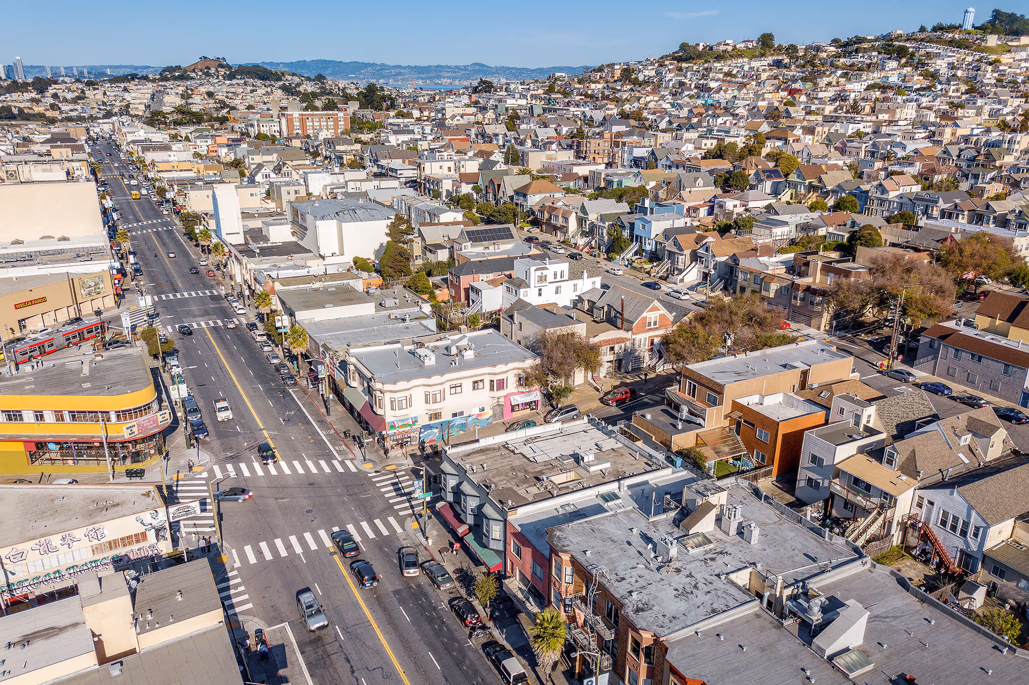 Aerial view of a cityscape with densely packed houses, streets, and cars, featuring a Wells Fargo building and distant hills.