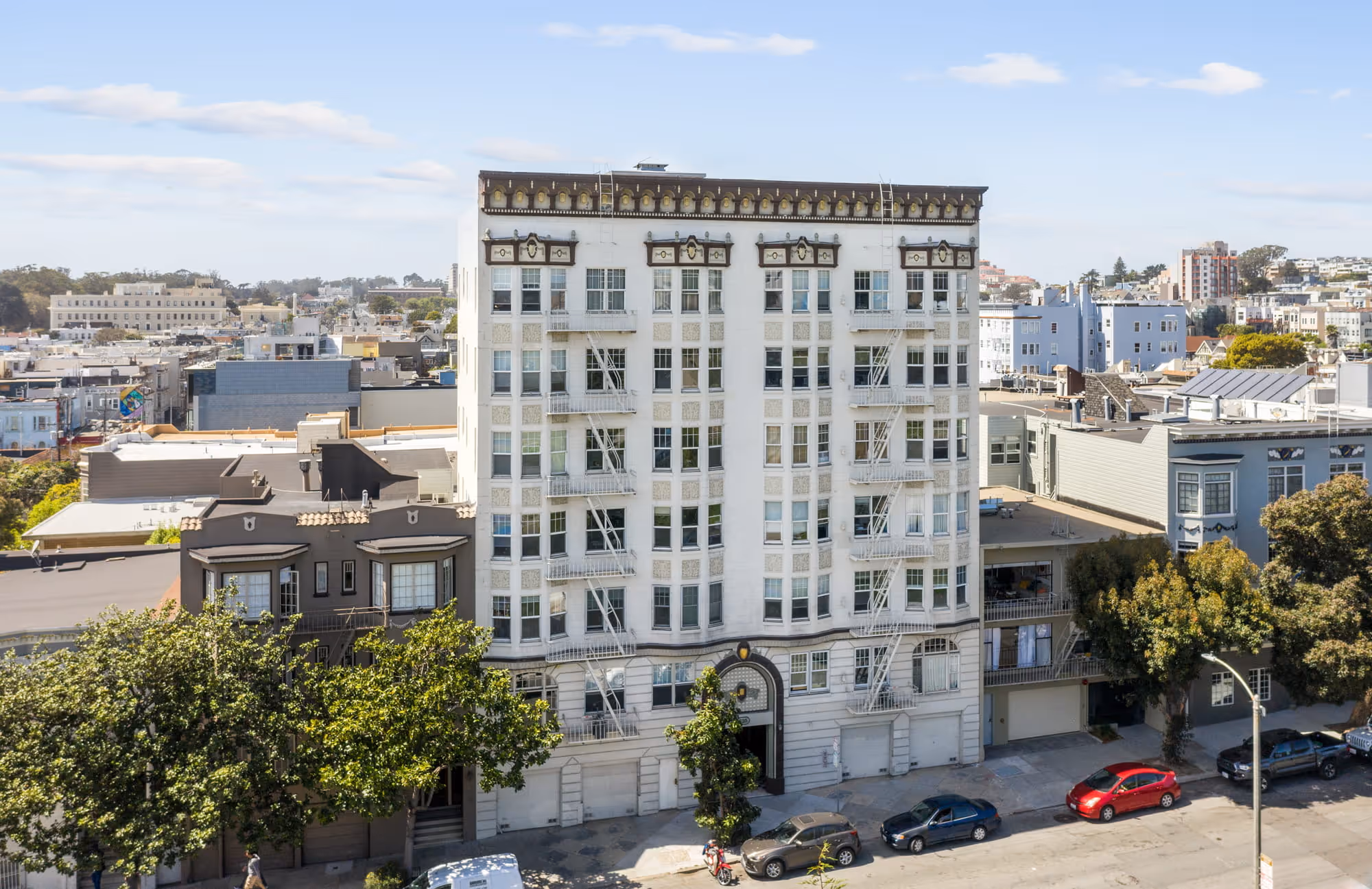White multi-story apartment building with multiple windows and fire escapes on a sunny day in an urban area.