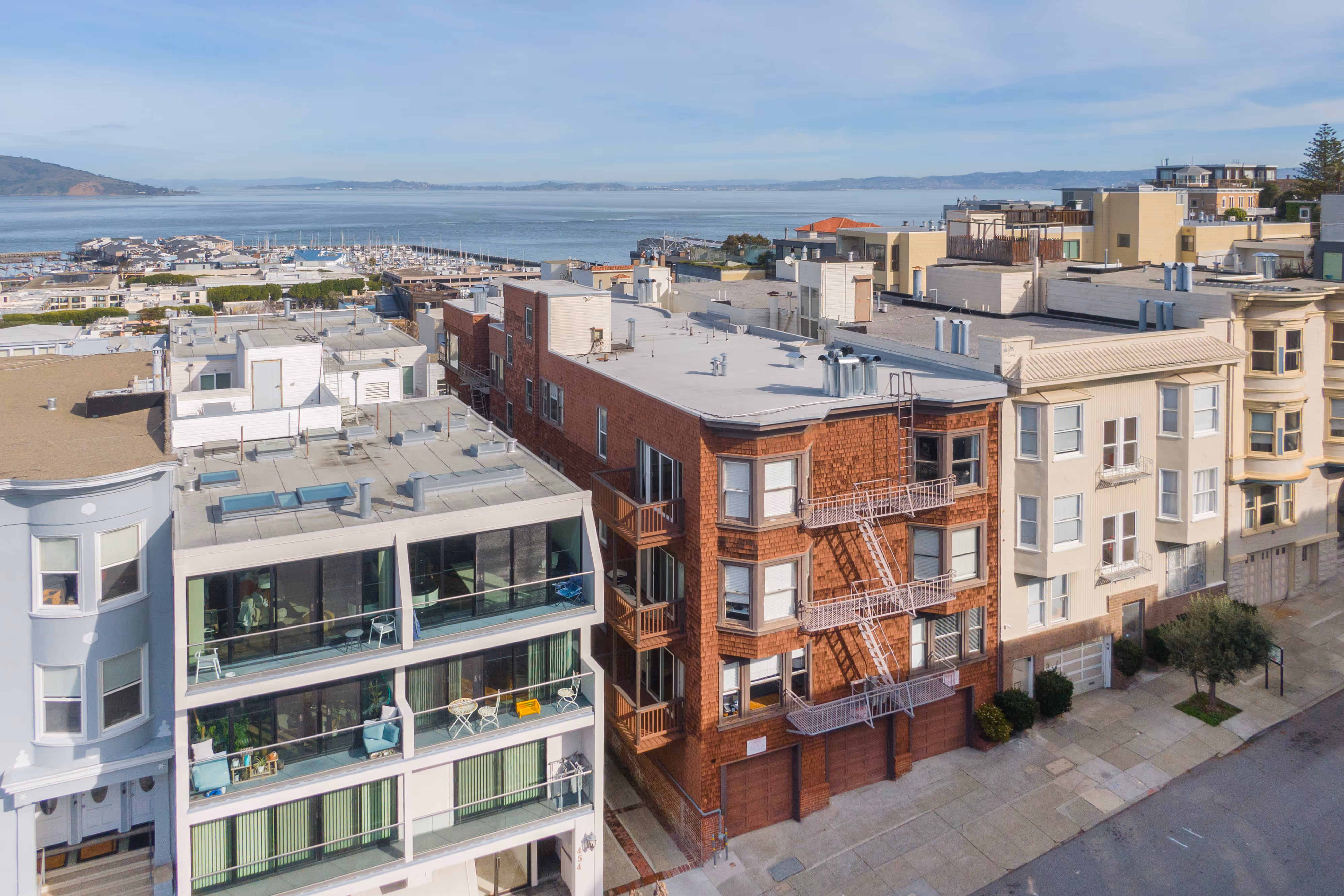 Aerial view of residential buildings near a waterfront with a marina and hills in the background under clear sky.