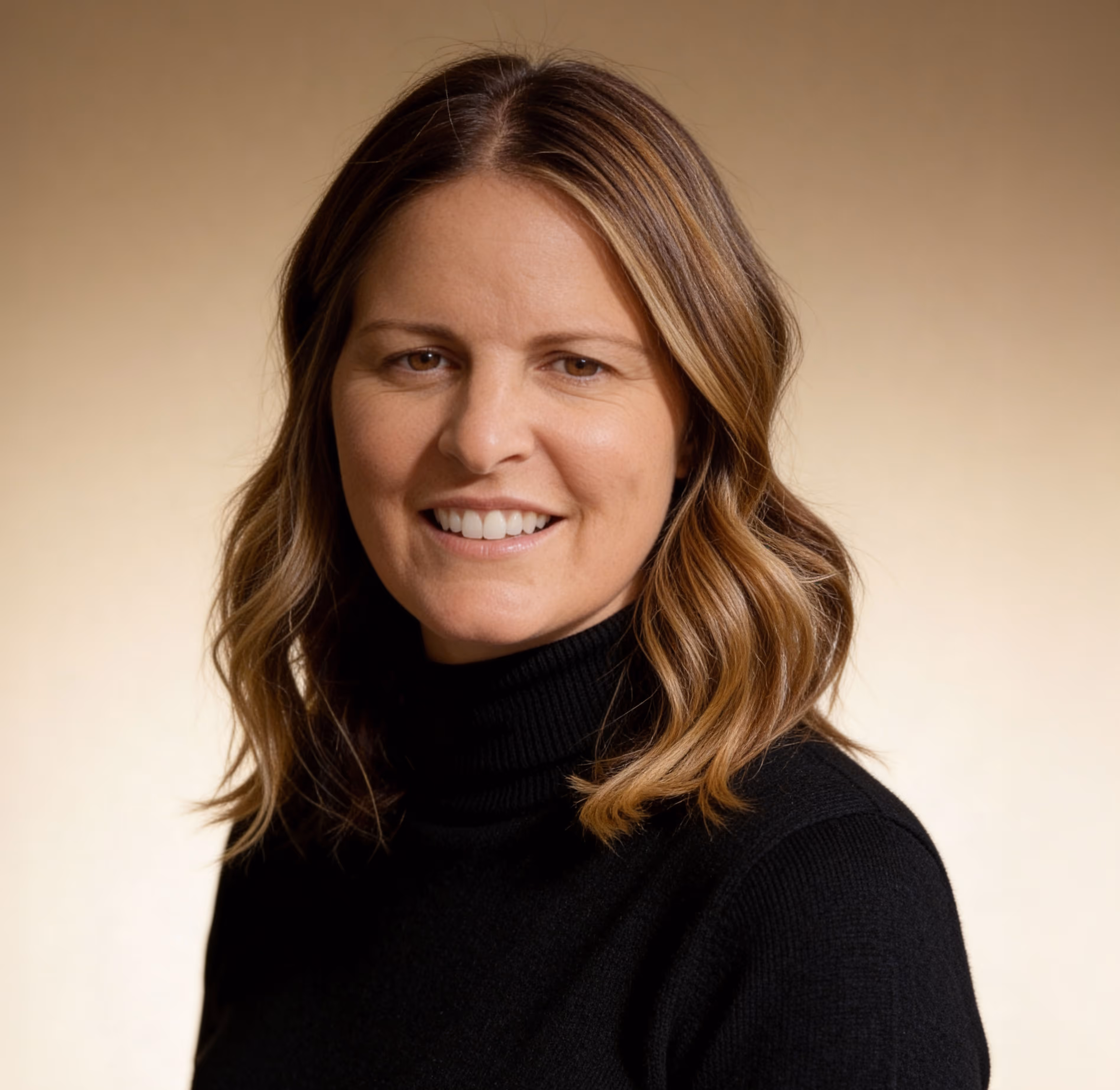 Smiling woman with shoulder-length brown hair wearing a black turtleneck against a beige background.