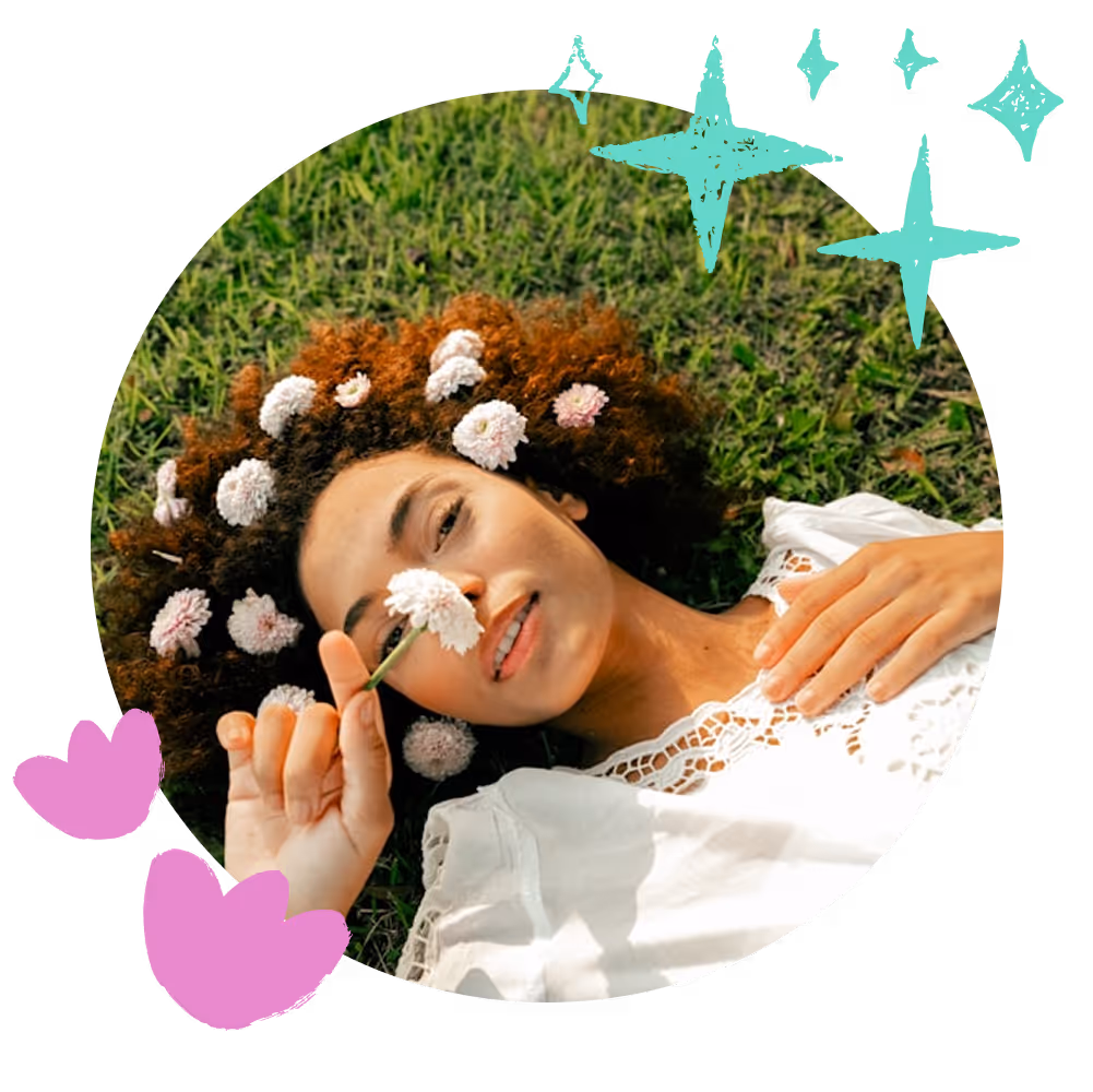 התמונה מציגה אישה שוכבת על הדשא, שערה מתמלא בפרחים לבנים קטנים. היא לובשת חולצה לבנה תחרתית ומחזיקה פרח סמוך לאפה בחיוך רגוע. סביב התמונה נוספו איורים צבעוניים – כוכבים טורקיזיים ולבבות ורודים – שמוסיפים תחושה חלומית ושובבה.