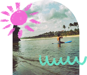 התמונה מציגה אישה יושבת על גלשן בלב הים, סמוך לחוף טרופי עם עצי דקל ושמיים מעוננים. מעל נוספו איורים צבעוניים – שמש ורודה וגלים טורקיז – המוסיפים לתמונה תחושה קלילה ושובבה.