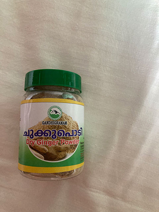 Jar of Gandhigram Dry Ginger Powder with a green cap on a light fabric surface.