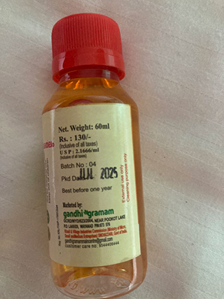 Small clear plastic bottle with orange liquid and red cap, label showing manufacturing and expiry dates, net weight 60ml.