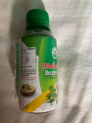 Small green-capped bottle of Brahmi oil with label showing plant image and usage instructions.