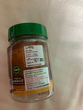 Clear jar with green lid containing ginger coffee powder, labeled with manufacturing details and a use-by date of October 2023.