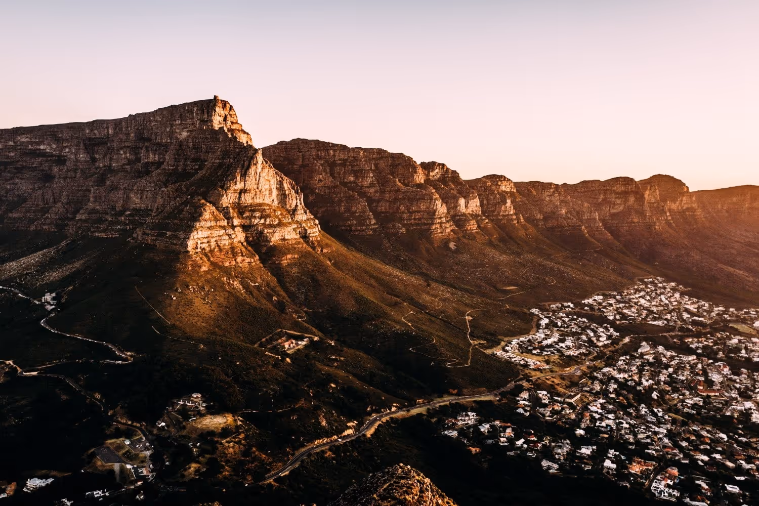 Mountain overlooking a sprawling city at sunset.