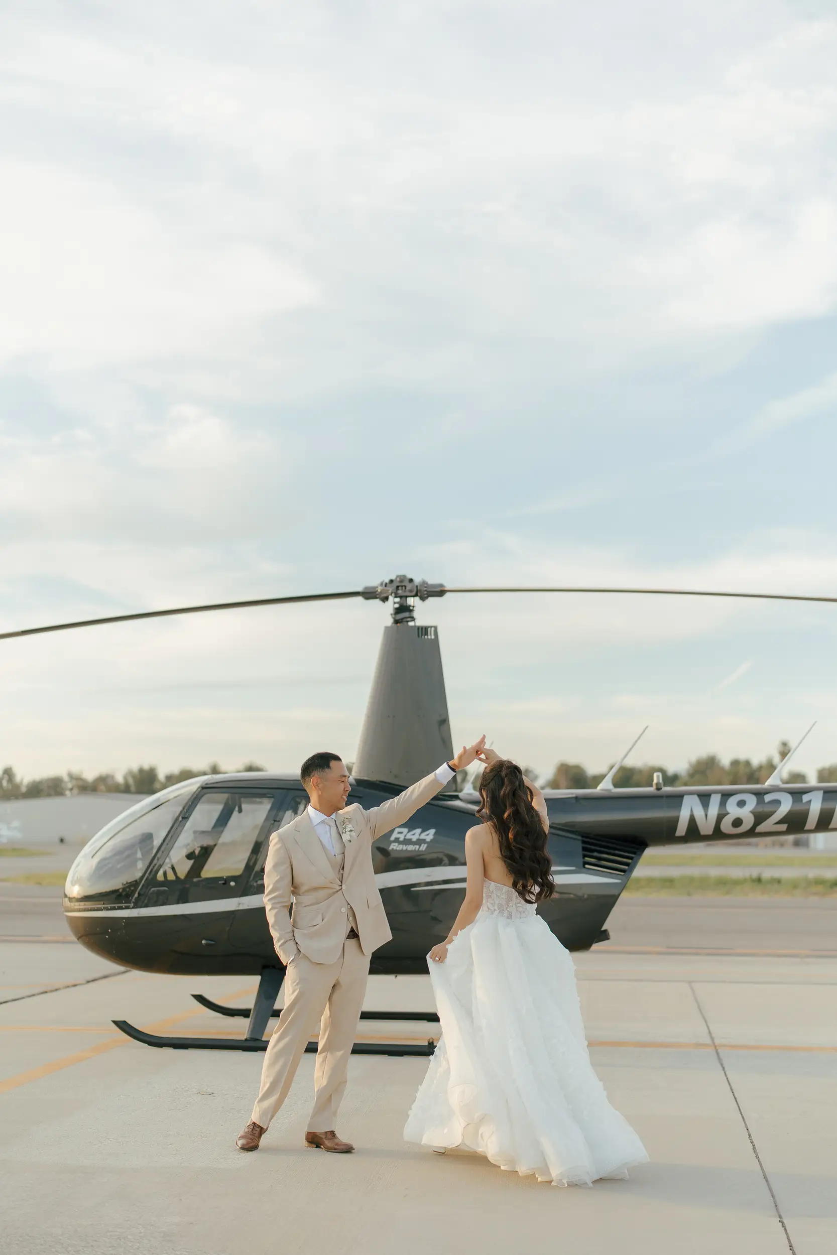 Bride and groom pose for photo in front of helicopter on the tarmac.