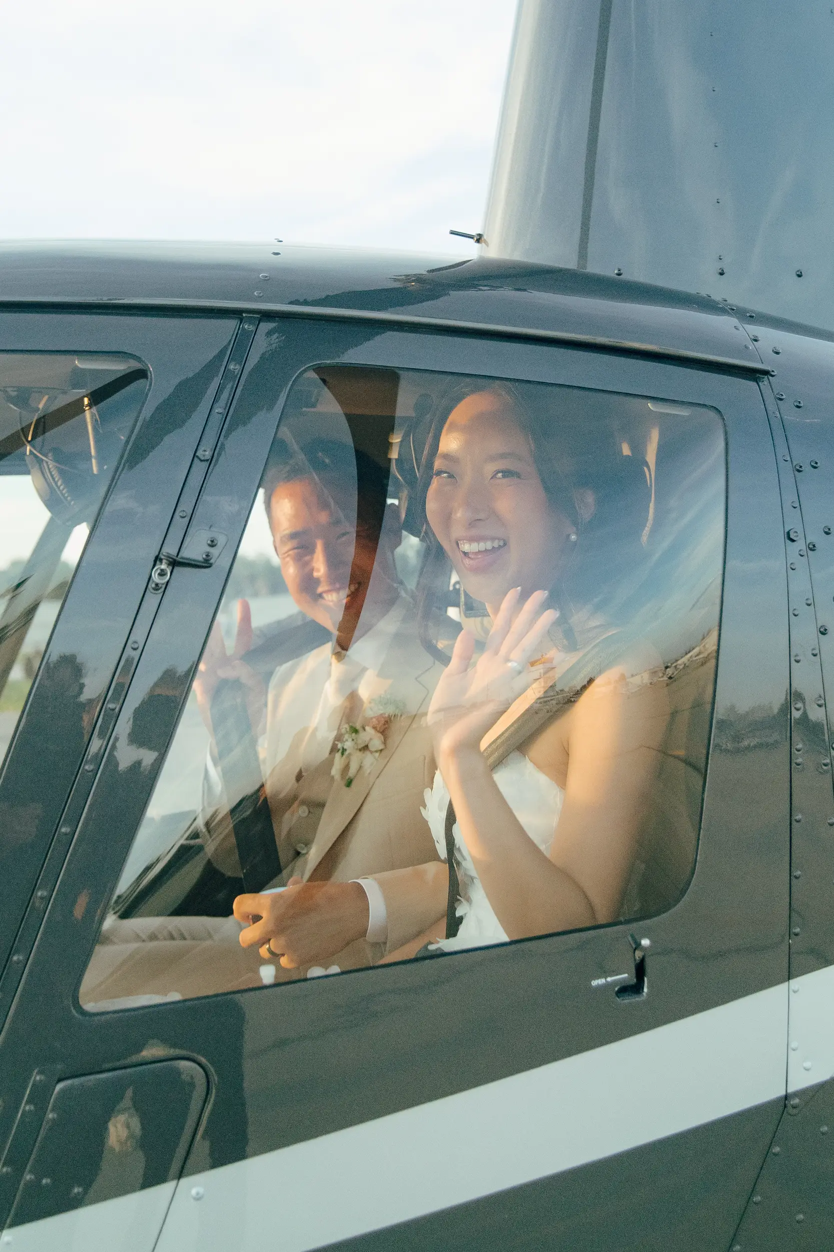 Bride and groom wave from inside helicopter before their flight.