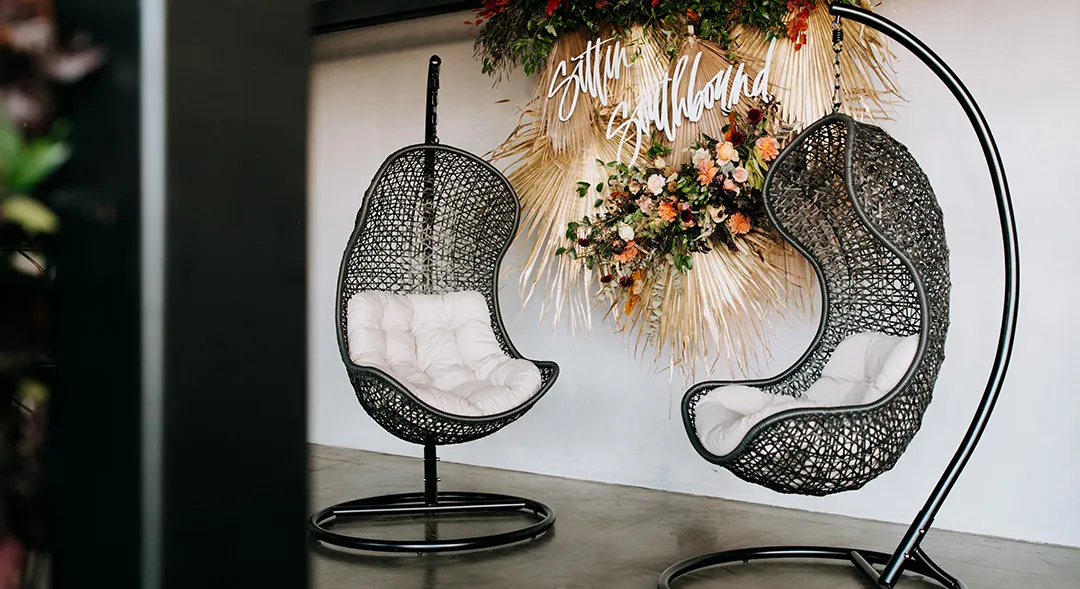 Two hanging chairs beside a floral backdrop inside Hangar 21