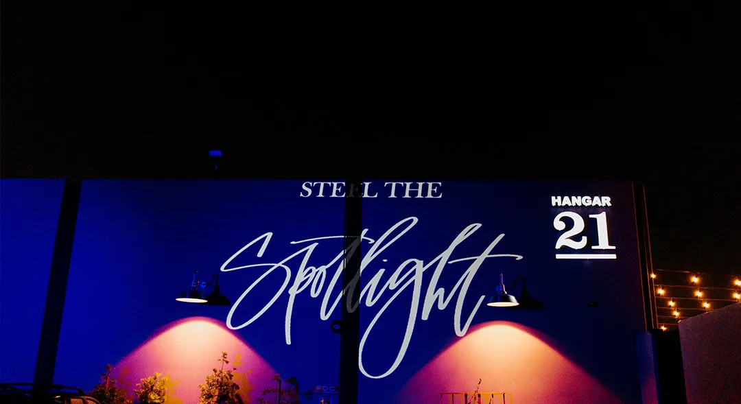 Steal the Spotlight lettering and Hangar 21 logo projected onto the hangar at night