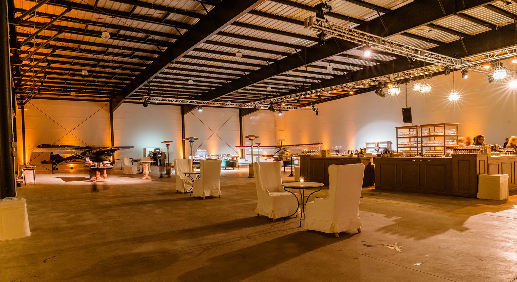 Cocktail tables, a bar and string lights inside the Executive Hangar