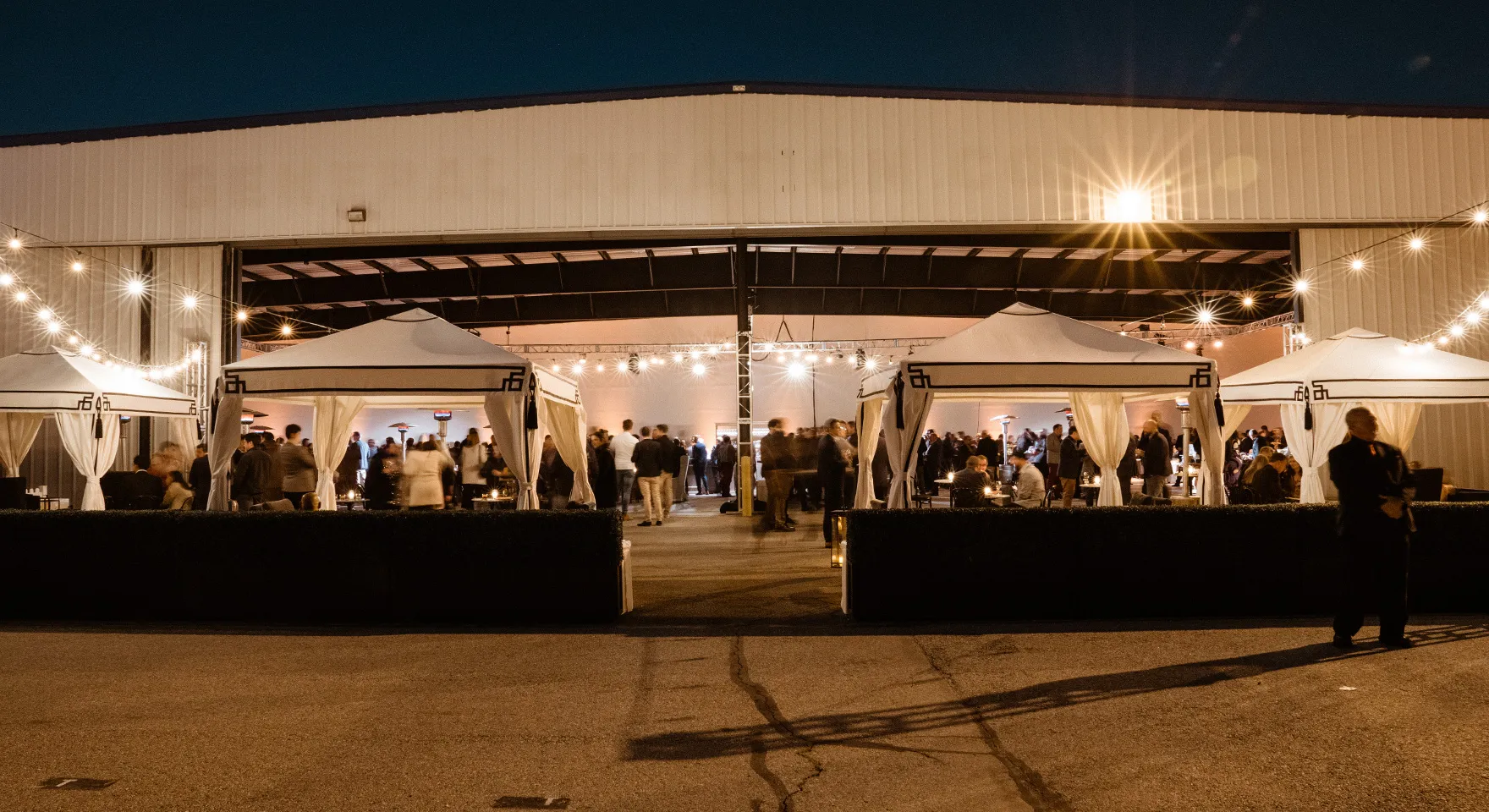 Evening reception beneath white canopies outside the Executive Hangar