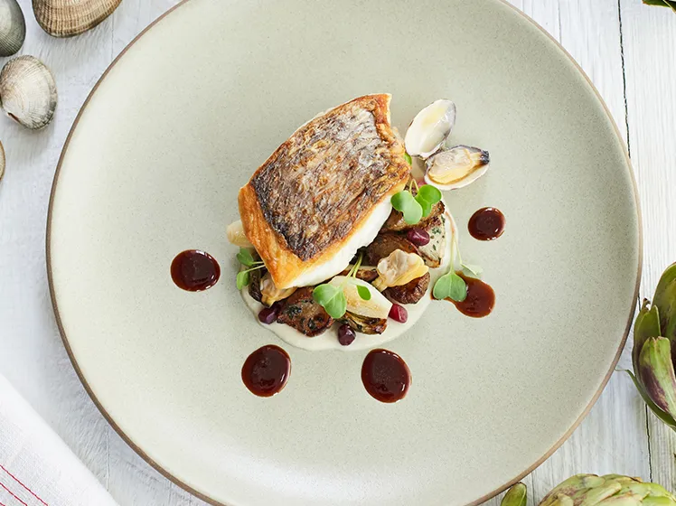 Seared fish fillet served with clams, vegetables and sauce