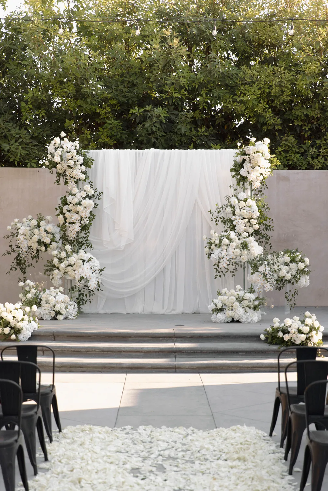 White wedding ceremony backdrop with draped fabric and white flowers.