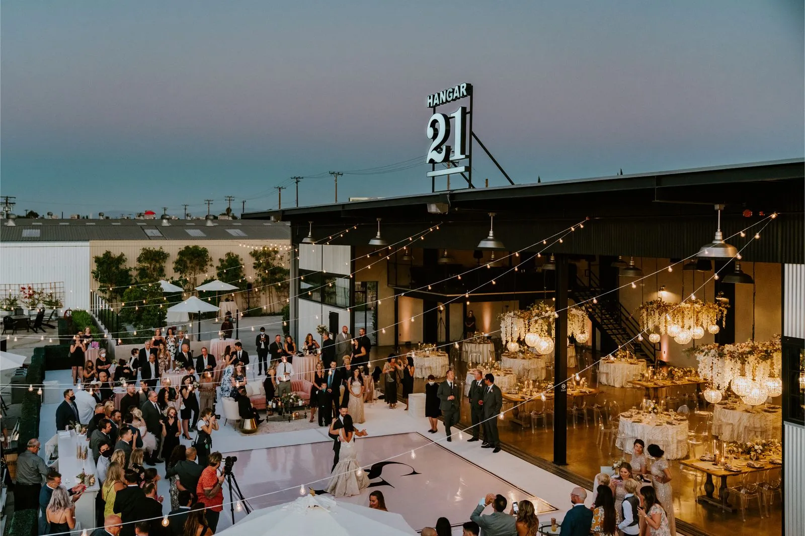 Wedding guests gathering outside the open Hangar 21 reception space at dusk
