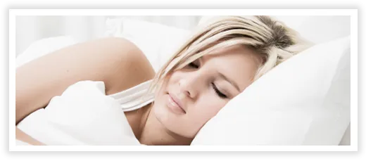 Woman with blonde hair peacefully sleeping on white pillows and bedding.