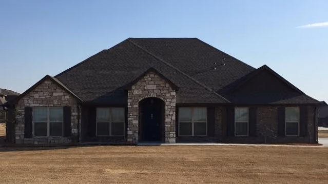 Single-story house with dark roof, stone and brick facade, four front windows, and an arched front door entrance.