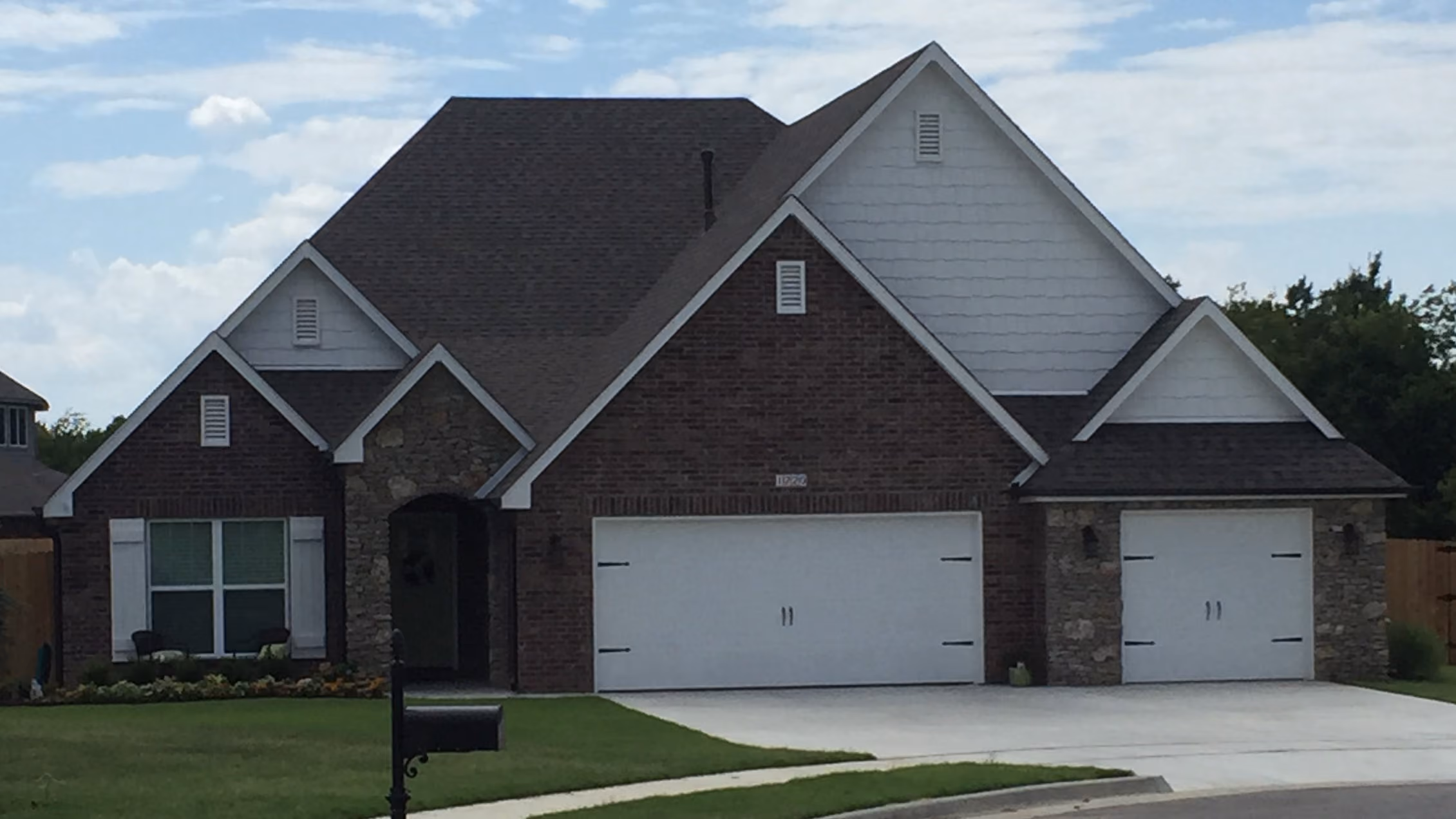 Single-story suburban house with brick and stone exterior, two white garage doors, and a mailbox in front.