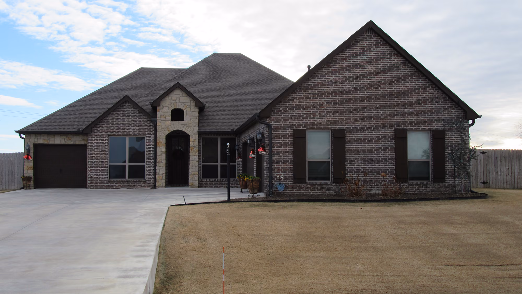 Single-story house with a large driveway, brick and stone exterior, and dark brown garage door and window shutters.