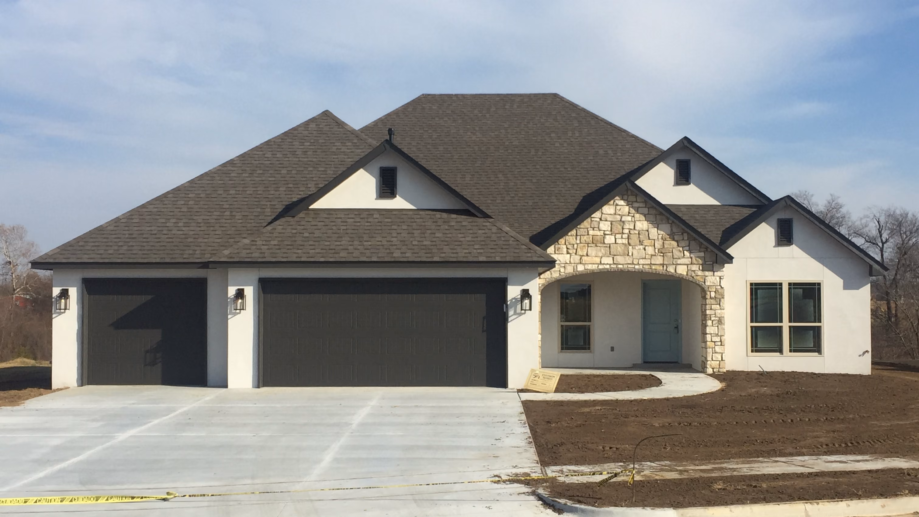 New single-story house with dark garage doors, stone arch entrance, and fresh concrete driveway.