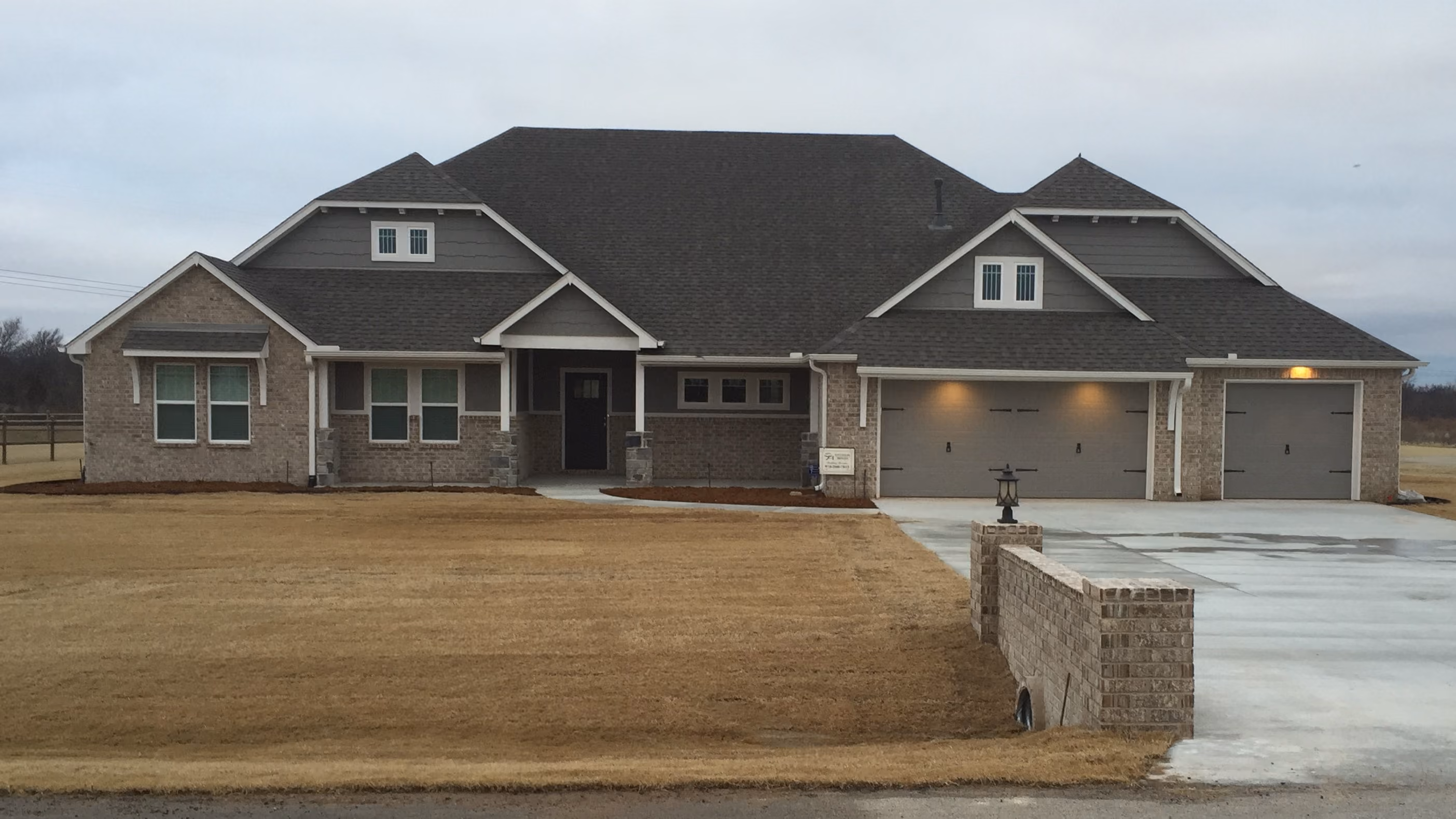 Single-story brick house with gray shingled roof, three garage doors, and extensive front lawn.
