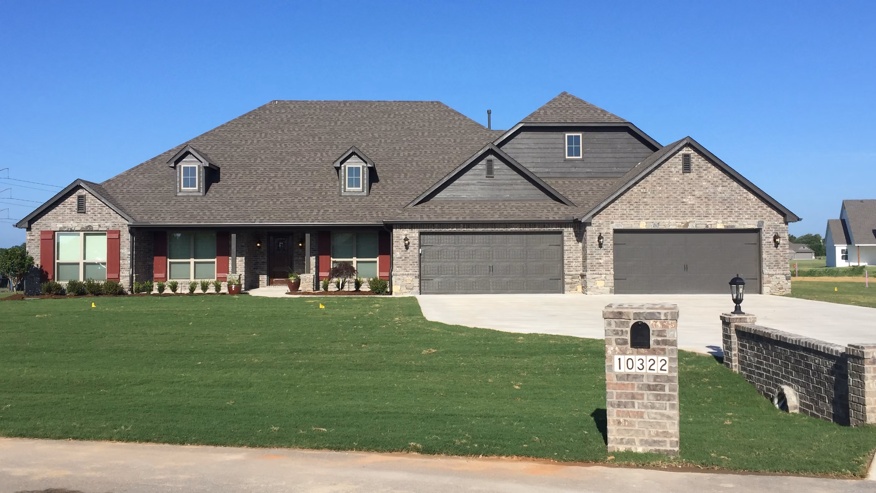 Single-story brick house with large front lawn, three garages, red window shutters, and mailbox displaying number 10322.