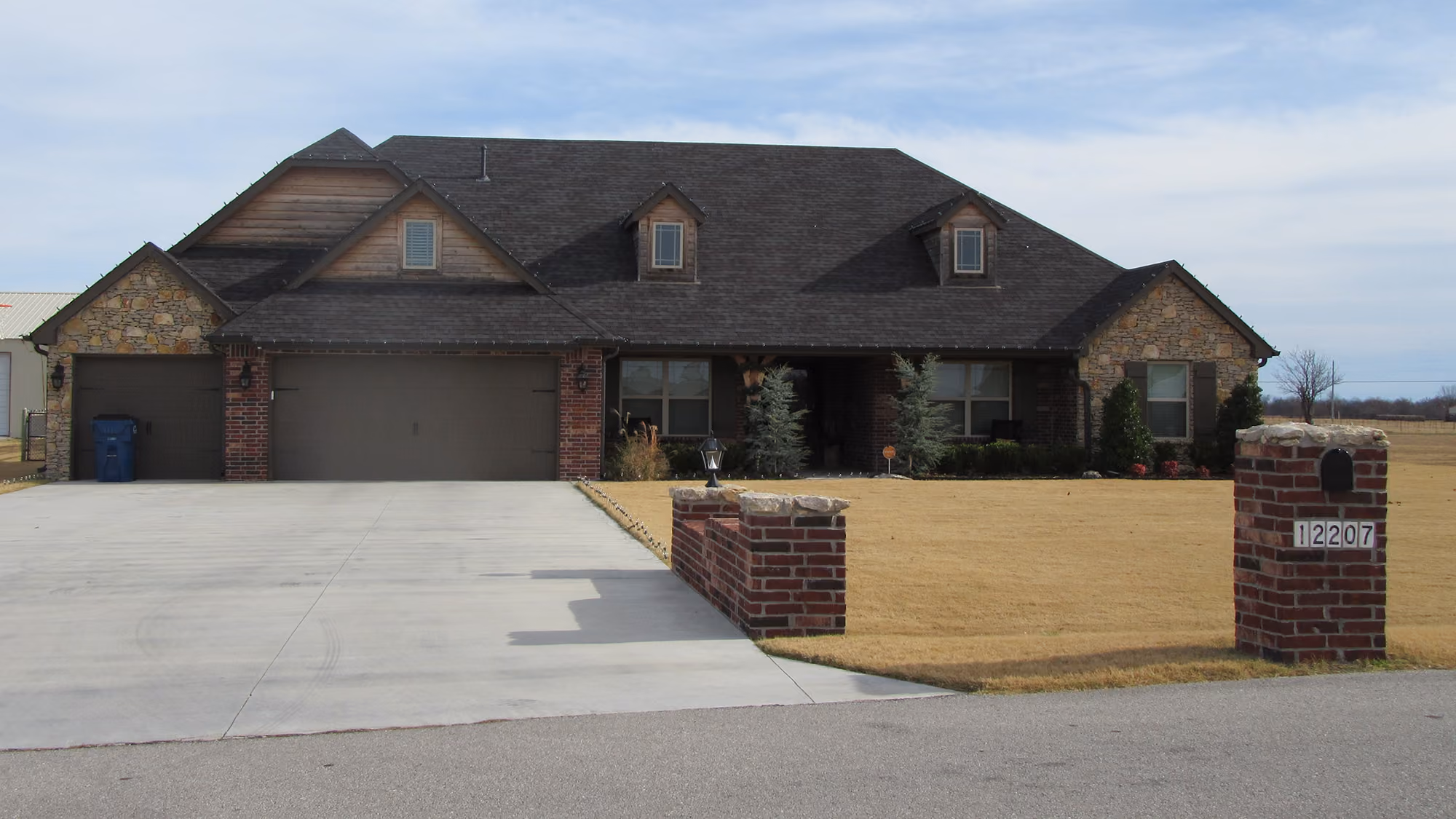 Single-story brick and stone house with a large driveway, three-car garage, and manicured lawn.