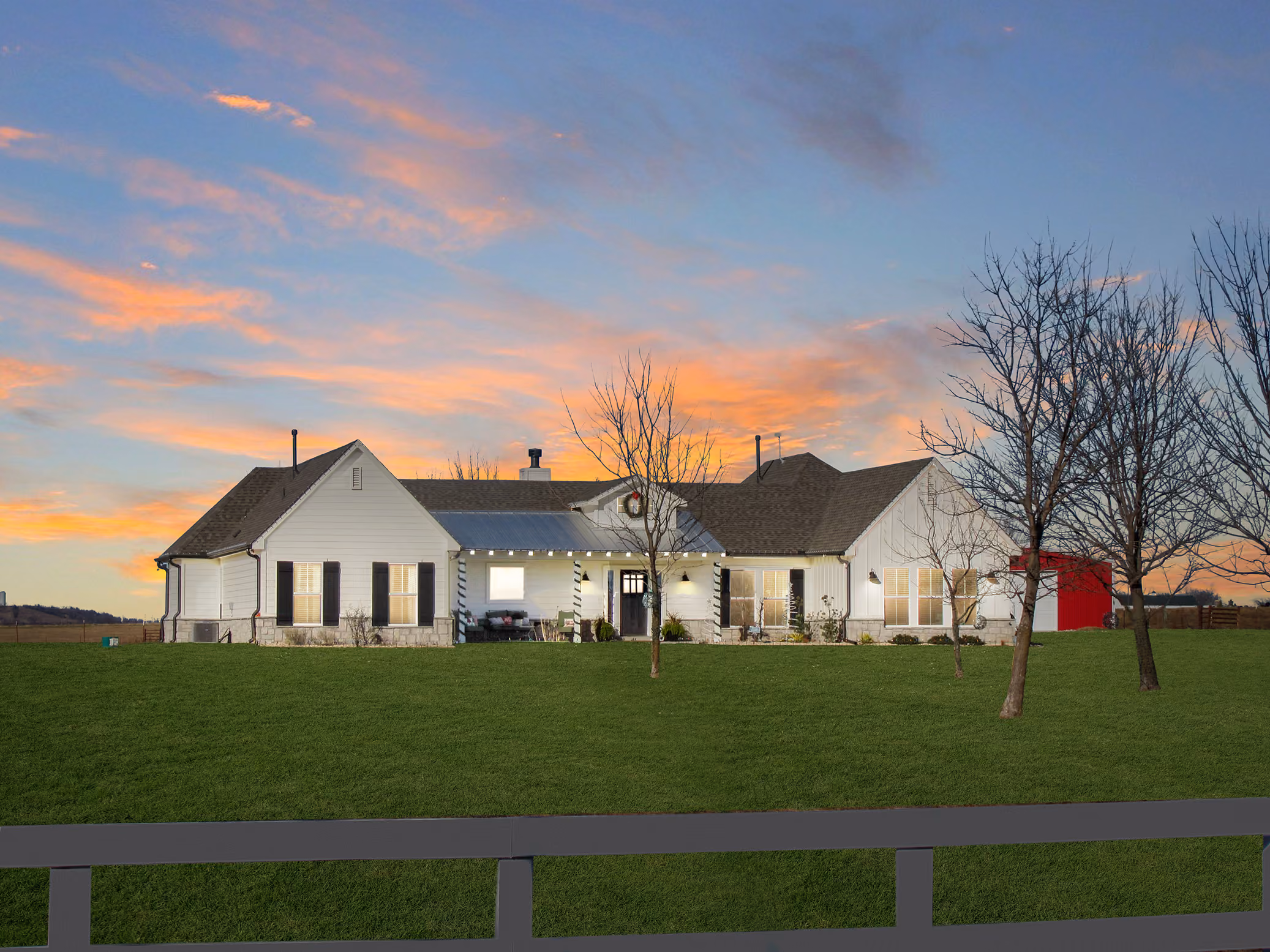 Large white single-story farmhouse with black shutters and a red barn door at sunset.